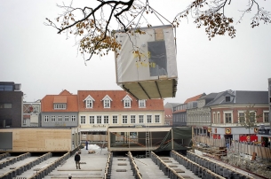 Svævende butikker. Store Torv bliver fra 1. november forvandlet til en butiksgade på cementklodser. Med to store mobilkraner bliver pavillionerne, der det næste halvandets års tid skal rumme butikkerne fra den gamle Danske Bank-bygning. sat på plads over parkeringskælderen. Pavillionerne kommer til Thisted på blokvogne der parkeres i svinget Jernbanegade-Toldbodgade. En mobilkran flytter pavillionerne højt over den gamle bankbygning til Store Torv. Mens pavillionerne hejses på plads bliver der arbejdet med at etablere el, vand og kloak. Butikkerne lukker fredag den 26. oktober og er klar igen torsdag den 1. november. Foto: Klaus Madsen